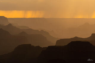 Sunset at Grand Canyon with layers of plateaus and monsoon storm clouds and rain.