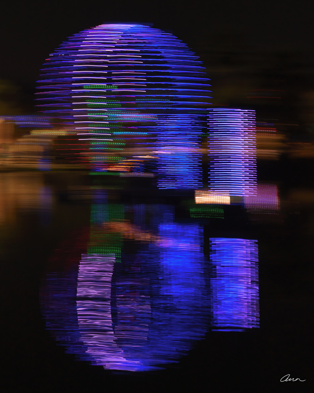 A sphere of neon lights reflects in a pond