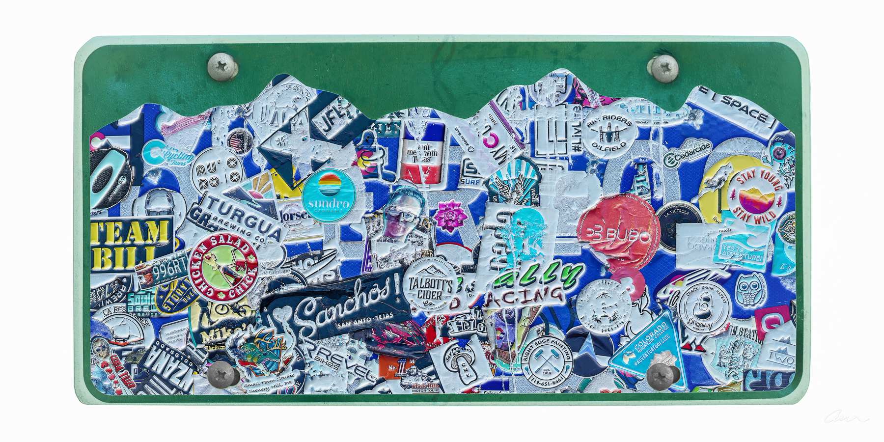 A Colorado license plate's mountain scene is covered with sticker culture.
